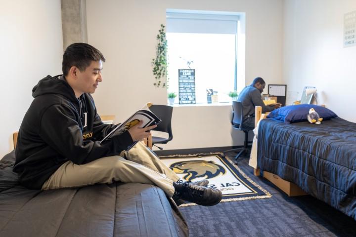 Student sitting on their bed reading, their roommate sits at a desk.
